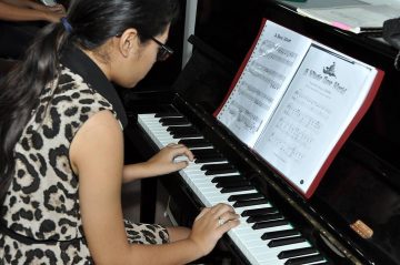 Een meisje speelt met twee handen op een zwarte akoestische piano.