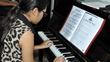 Een meisje speelt met twee handen op een zwarte akoestische piano.