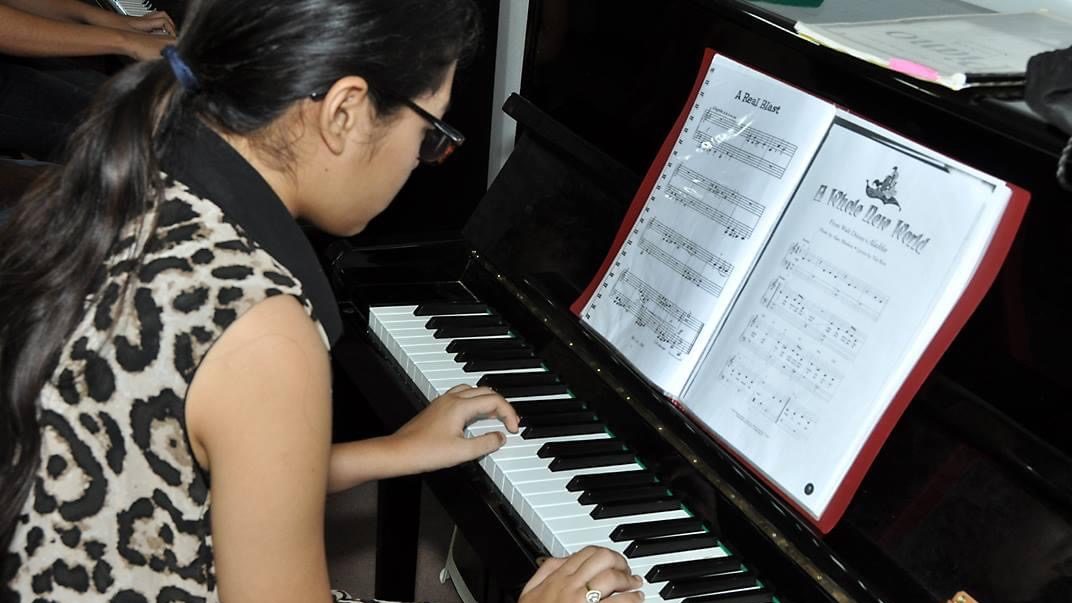 Een meisje speelt met twee handen op een zwarte akoestische piano.